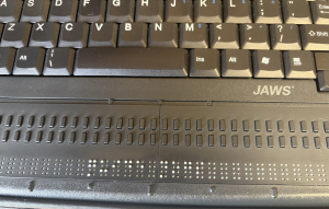 A photo of an electronic Braille device connected to my PAC Mate Omni&trade; displaying the words “Guide Dogs”